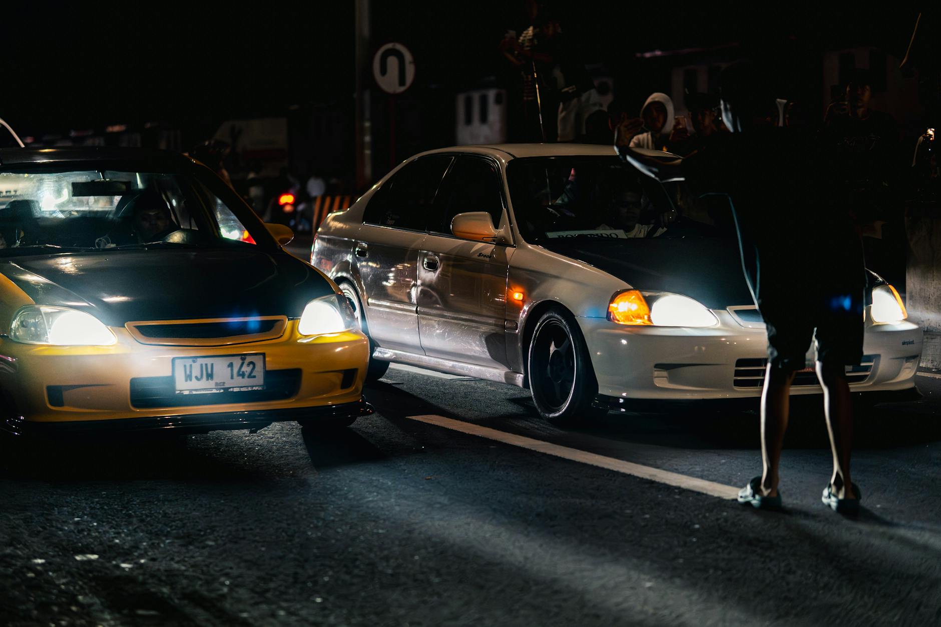 Dramatic night shot capturing street car racing with onlookers and vivid headlights.
