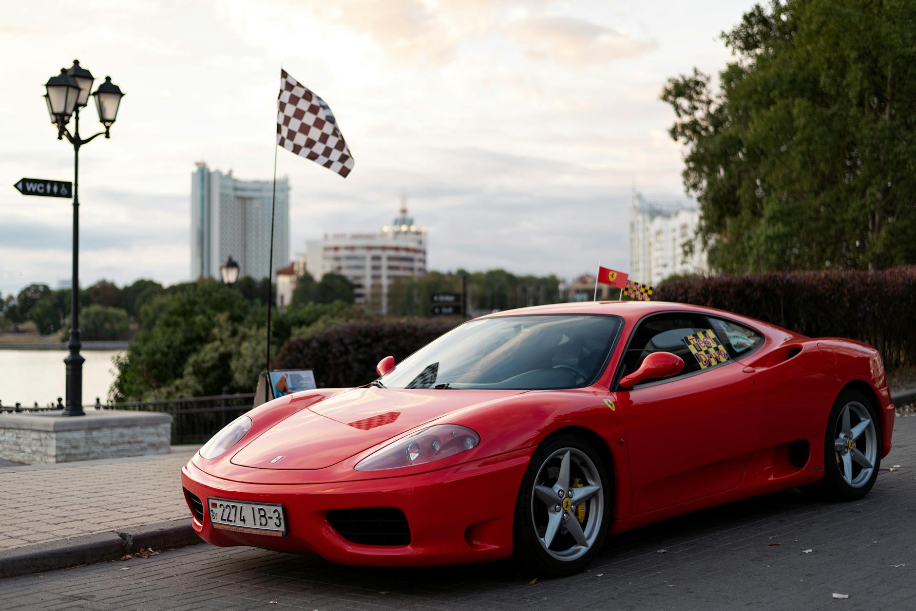 High-end red sports car parked outdoors with checkered flag and city backdrop.
