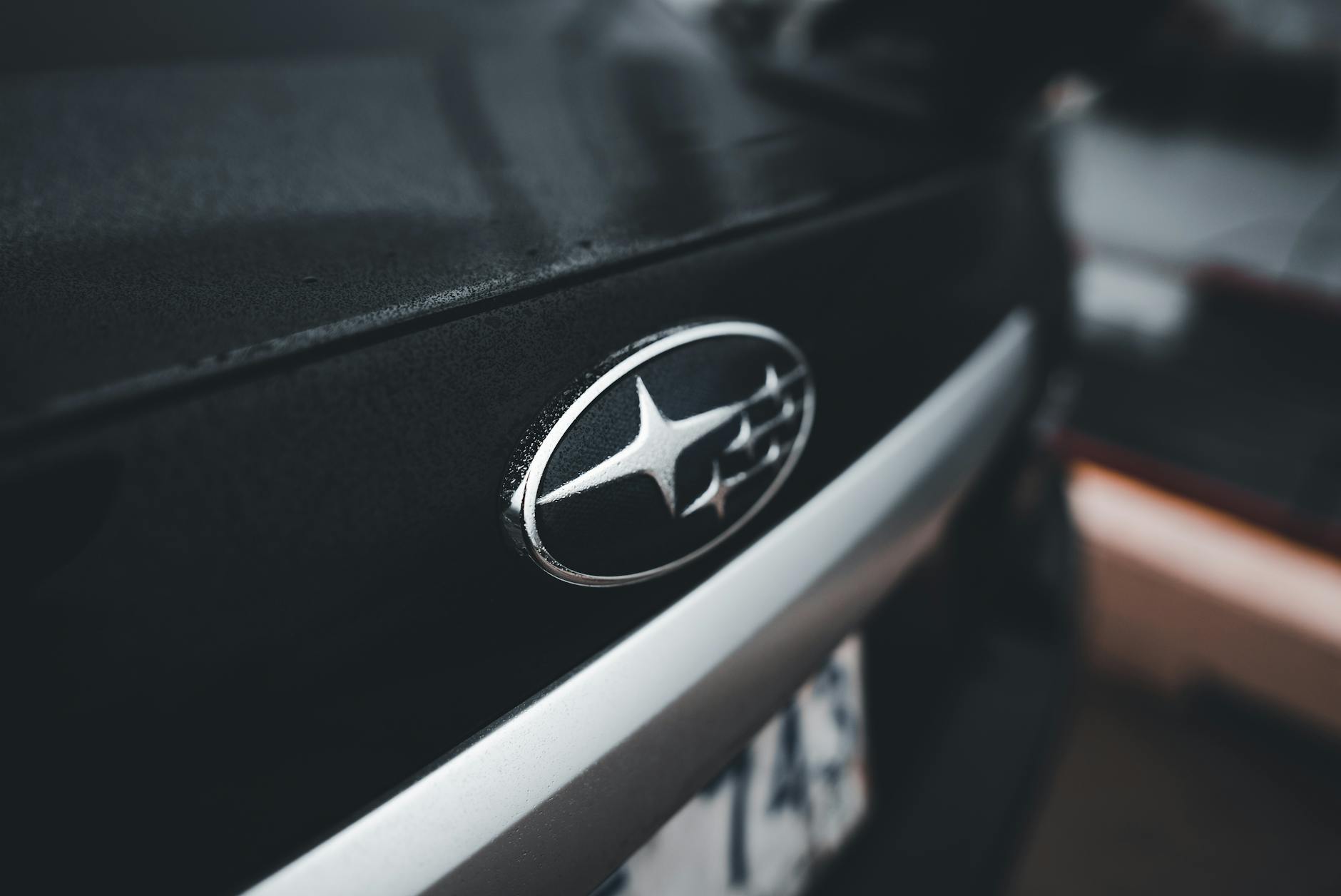 Detailed close-up of a Subaru car emblem on a wet black vehicle trunk, showcasing automotive design.