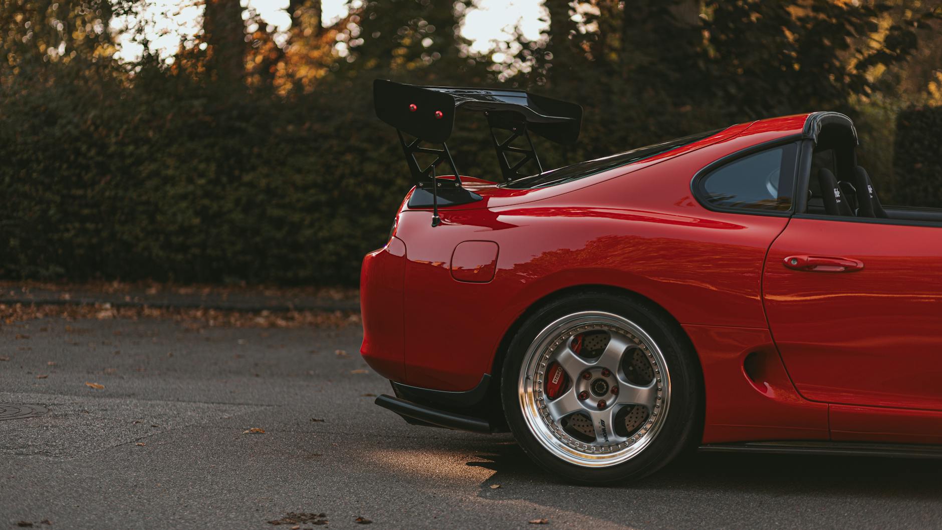 A striking red sports car showcasing a custom rear spoiler and shiny alloy wheels in an outdoor setting.