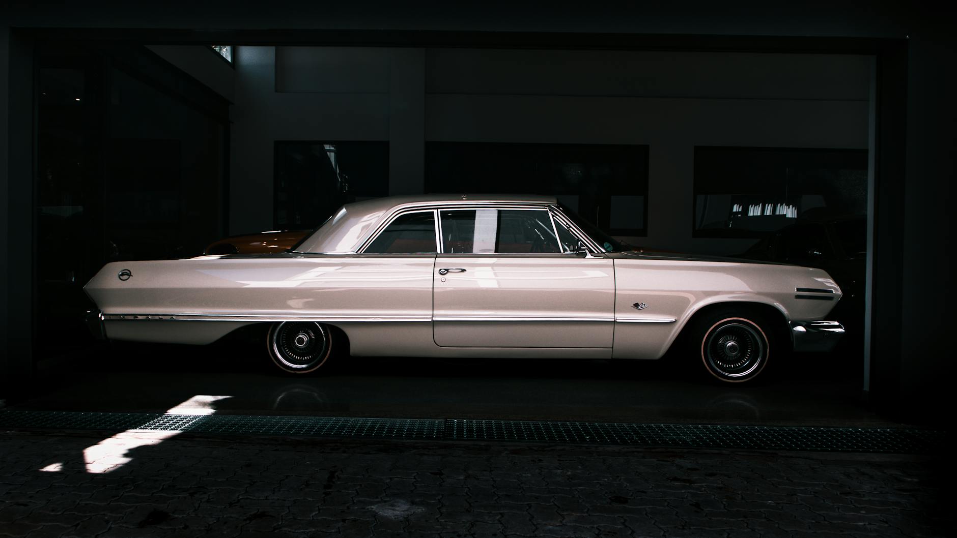 Side view of a vintage classic car in a dimly lit garage, highlighting its sleek design.