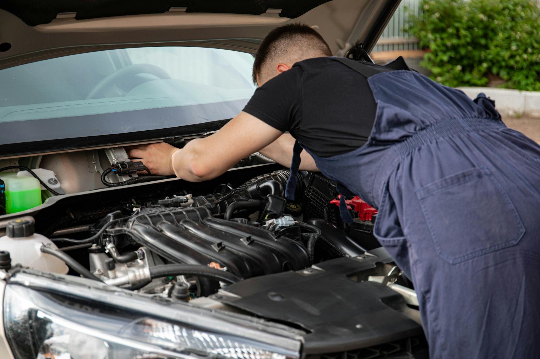 A mechanic performing maintenance work on a car's engine in an outdoor setting.