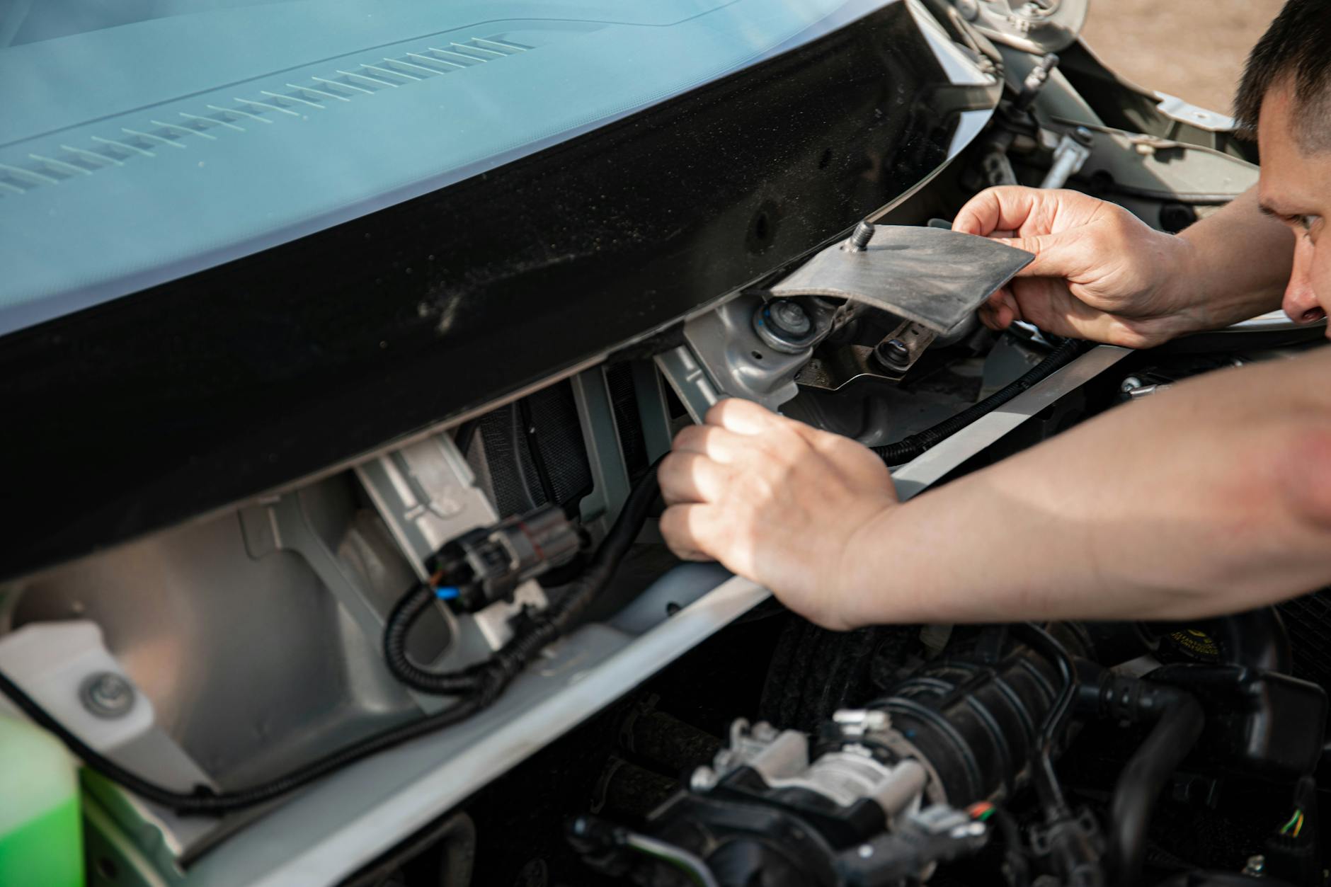 Close-up of a mechanic working on a car engine outdoors in bright daylight.