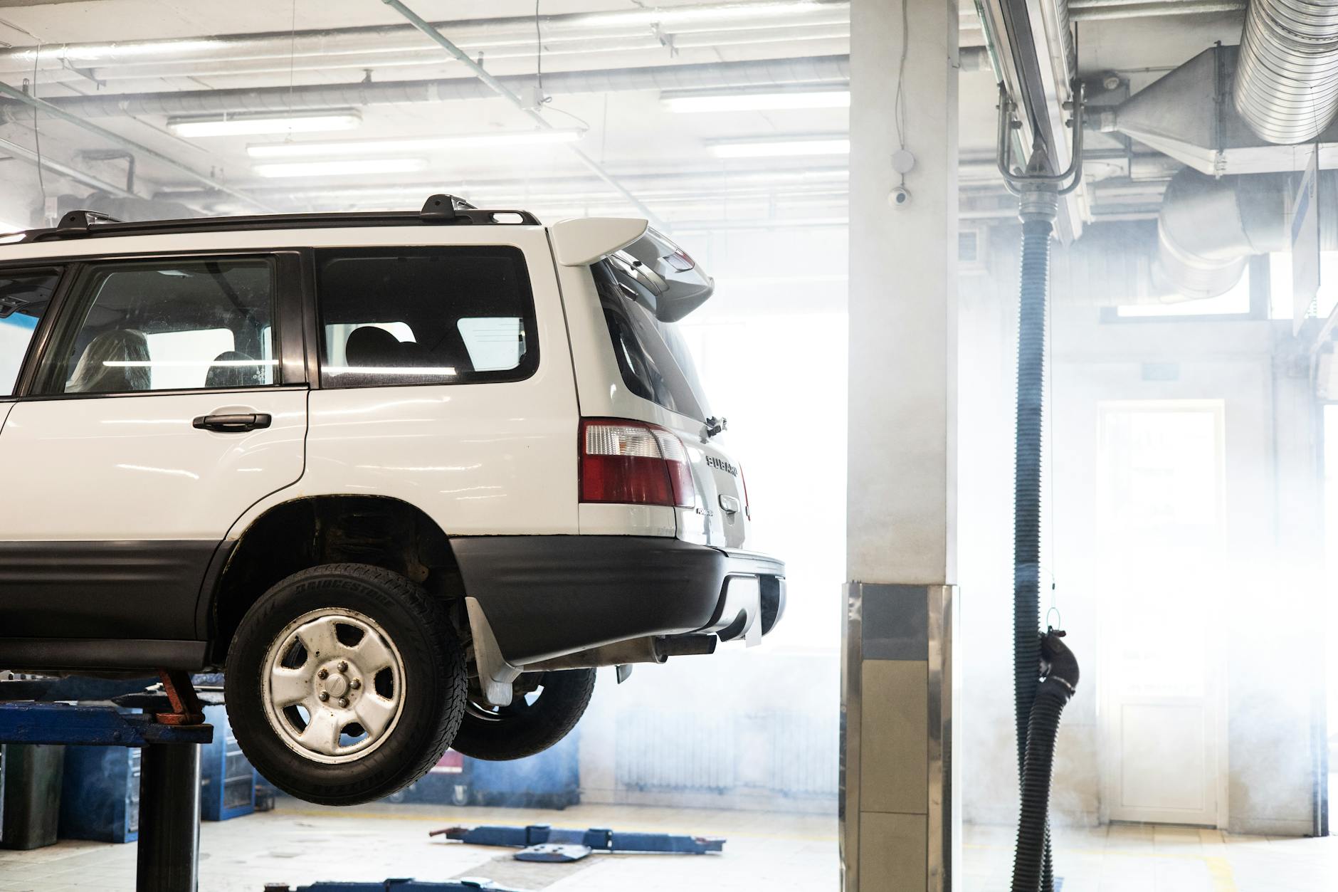 A white SUV is elevated on a lift inside an auto repair shop for maintenance.