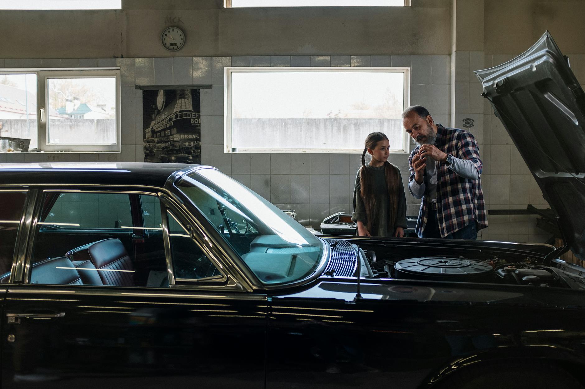 Father explains car mechanics to daughter in an auto repair shop. A moment of learning and bonding.