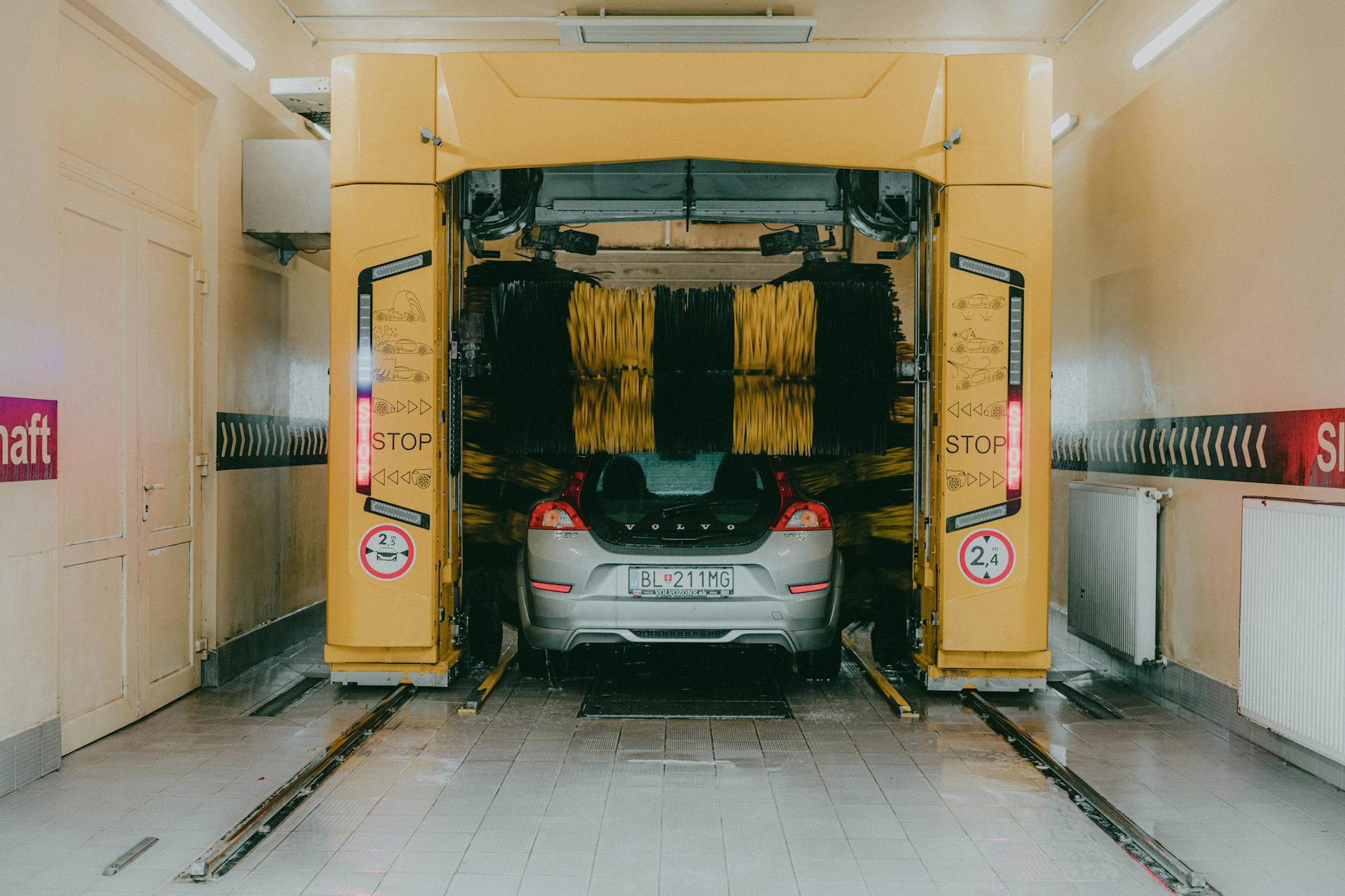 A car undergoing a cleaning process in an automated car wash station with a yellow gantry machine.
